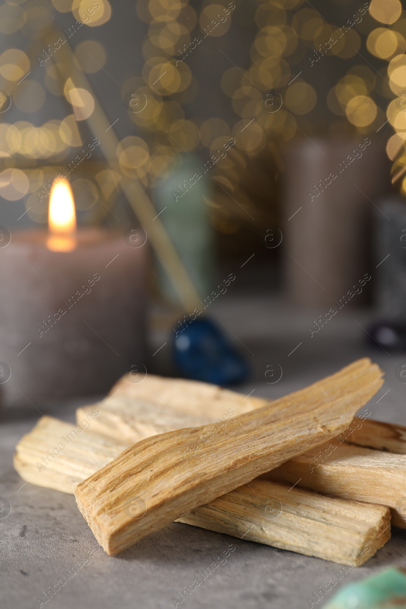 Photo of Palo santo sticks and gemstones on grey table against blurred lights, closeup