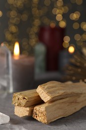 Photo of Palo santo sticks and gemstone on grey table against blurred lights, closeup