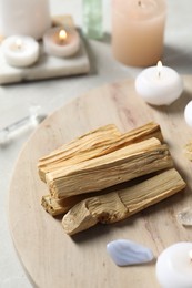 Photo of Palo santo sticks, gemstones and burning candles on light table, closeup