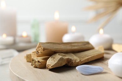 Photo of Palo santo sticks, gemstones and burning candles on light table, closeup