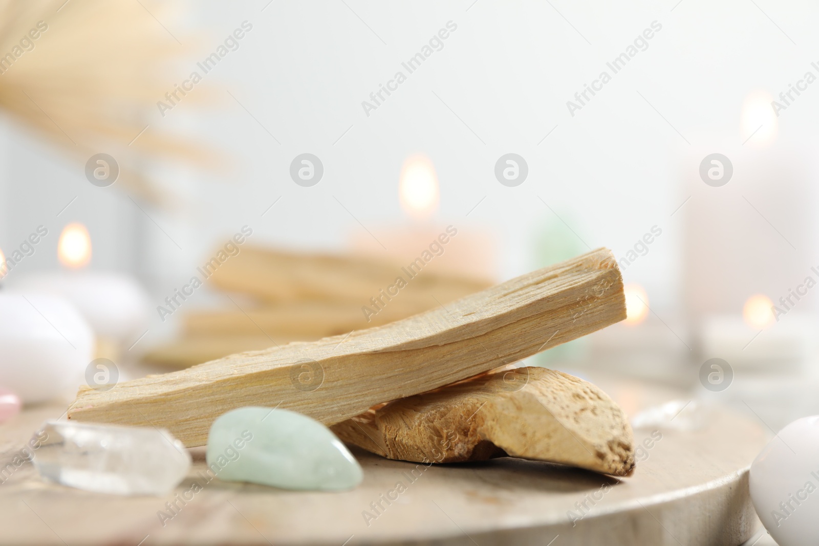 Photo of Palo santo sticks, gemstones and burning candles on light table, closeup