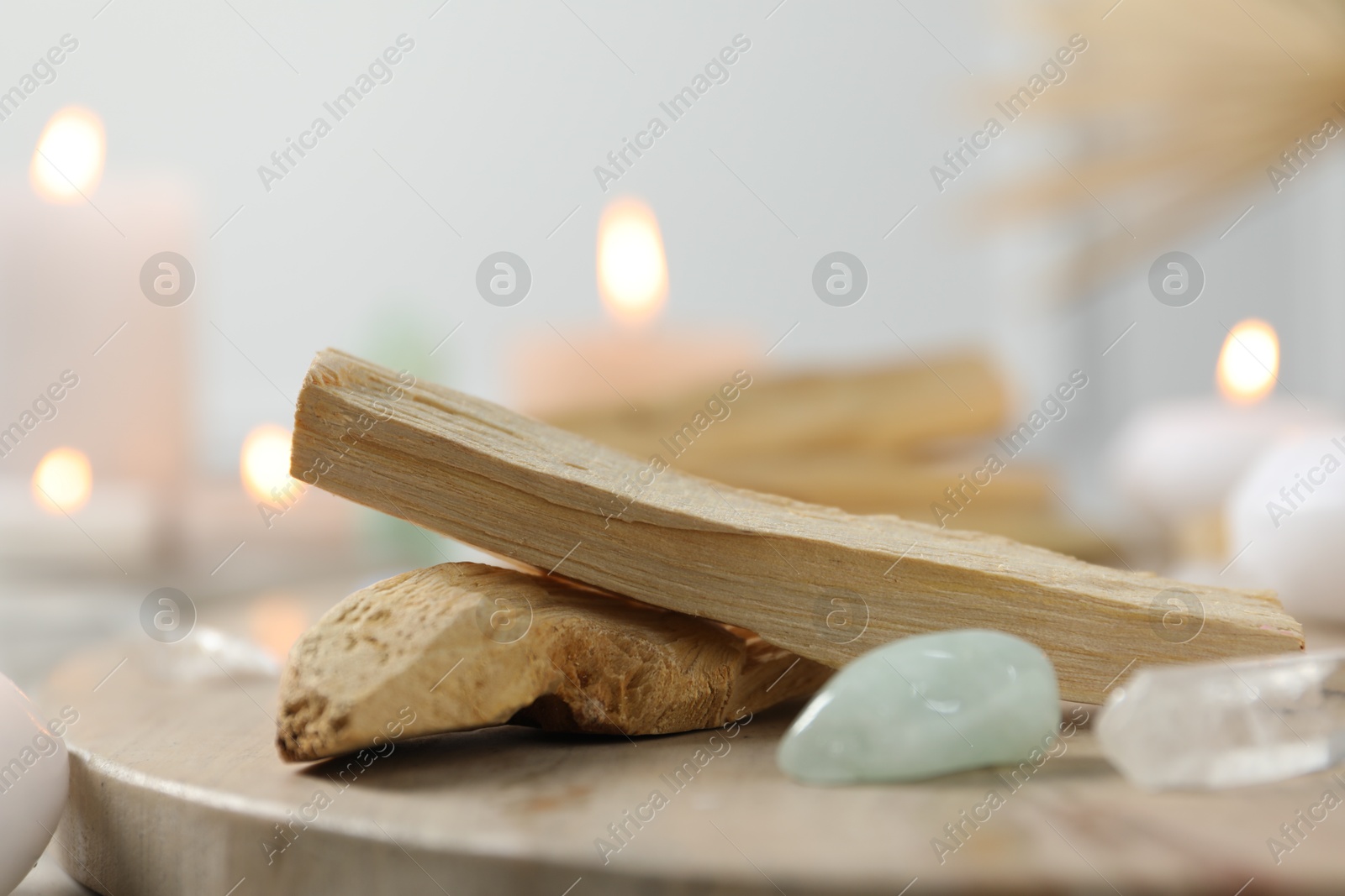 Photo of Palo santo sticks, gemstones and burning candles on light table, closeup