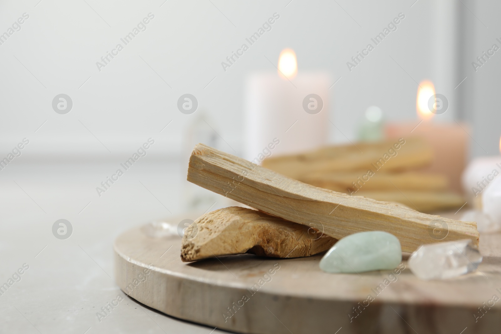 Photo of Palo santo sticks, gemstones and burning candles on light table, closeup