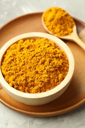 Photo of Turmeric powder in bowl and spoon on light grey table, closeup