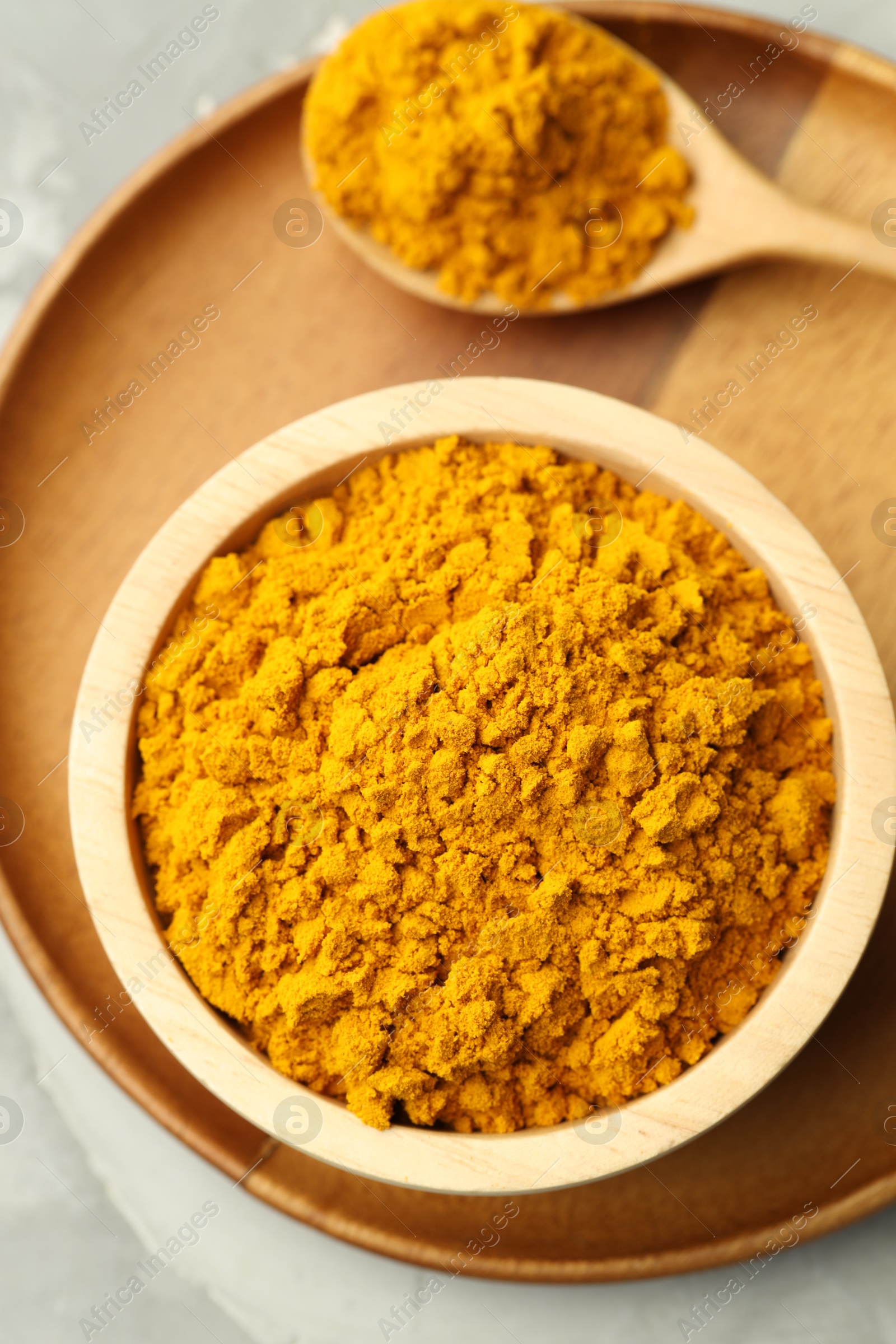 Photo of Turmeric powder in bowl and spoon on light grey table, top view