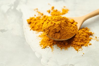 Photo of Turmeric powder and spoon on light grey table, closeup. Space for text