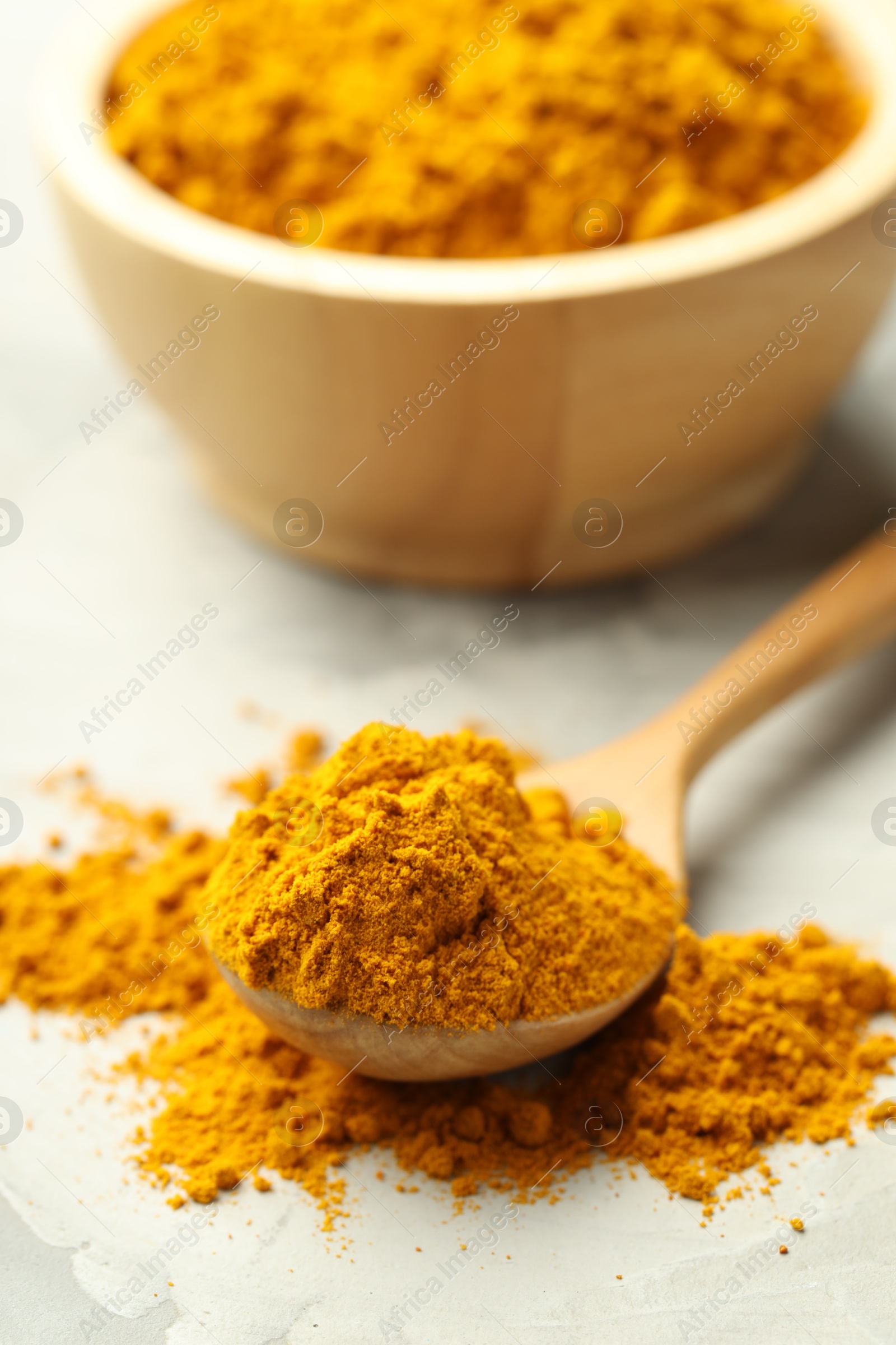 Photo of Turmeric powder and spoon on light grey table, closeup