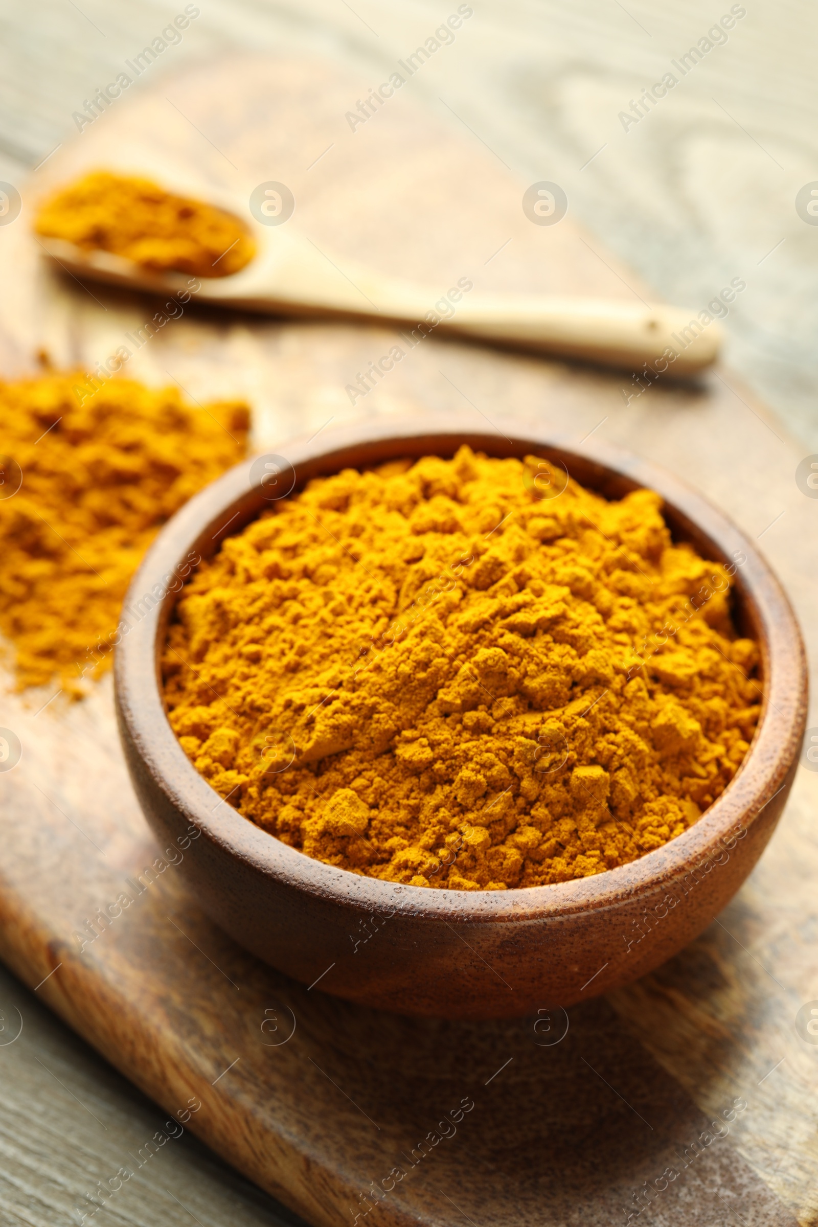 Photo of Turmeric powder in bowl on wooden table, closeup