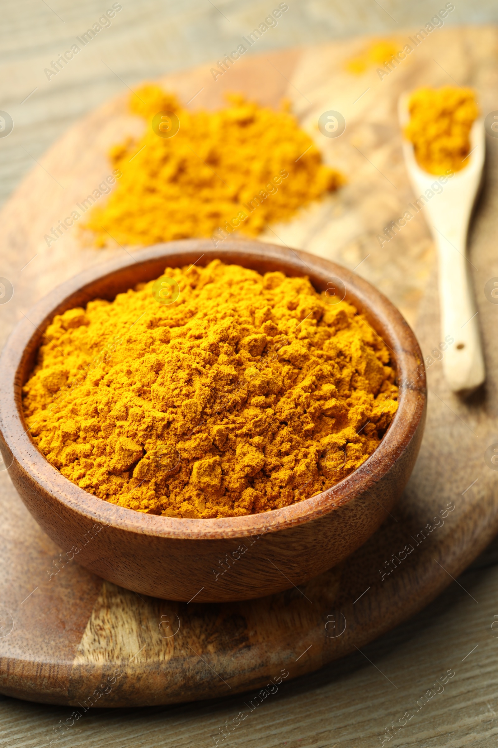 Photo of Turmeric powder in bowl on wooden table, closeup