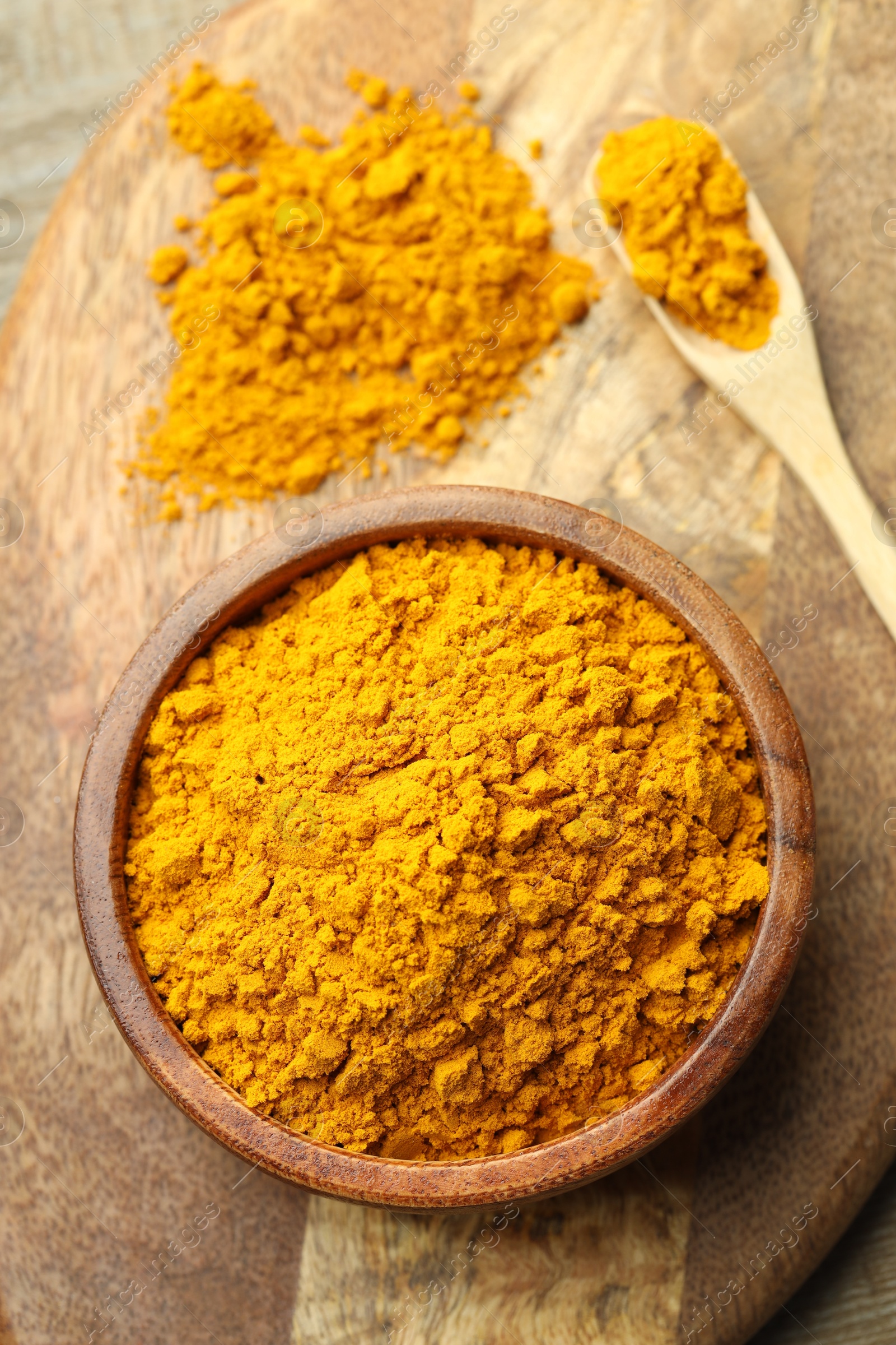 Photo of Turmeric powder in bowl and spoon on table, top view