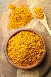 Photo of Turmeric powder in bowl and spoon on table, top view