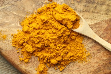 Photo of Turmeric powder and spoon on wooden table, above view