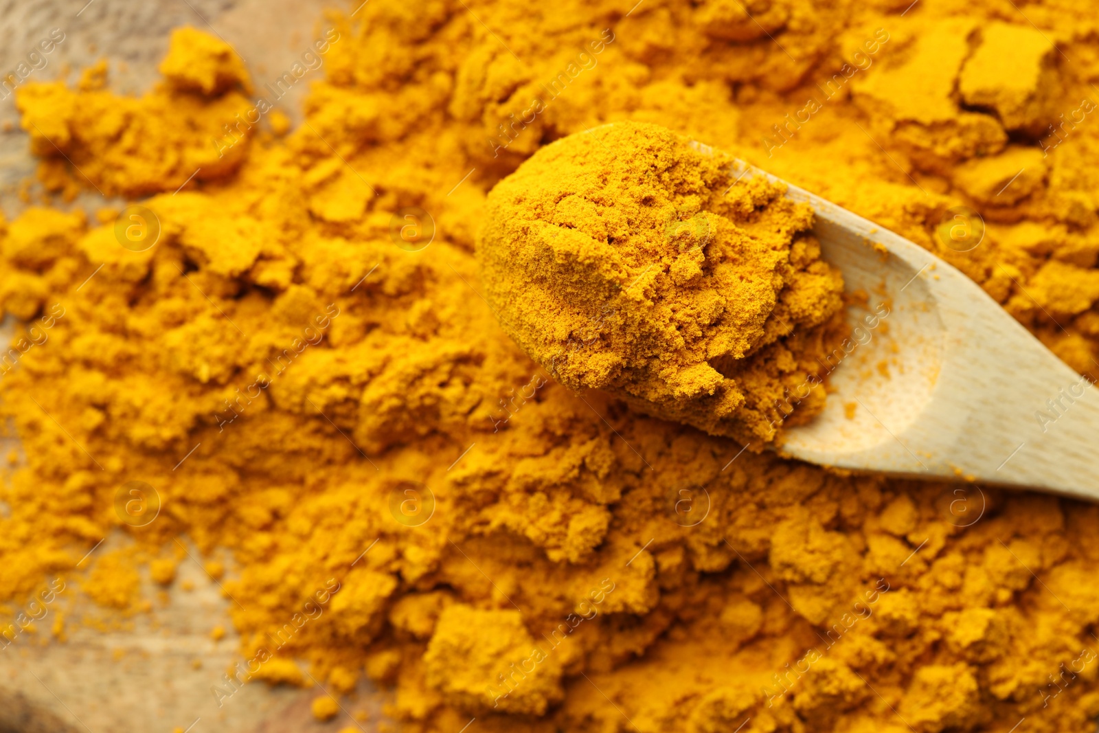 Photo of Turmeric powder and spoon on table, closeup