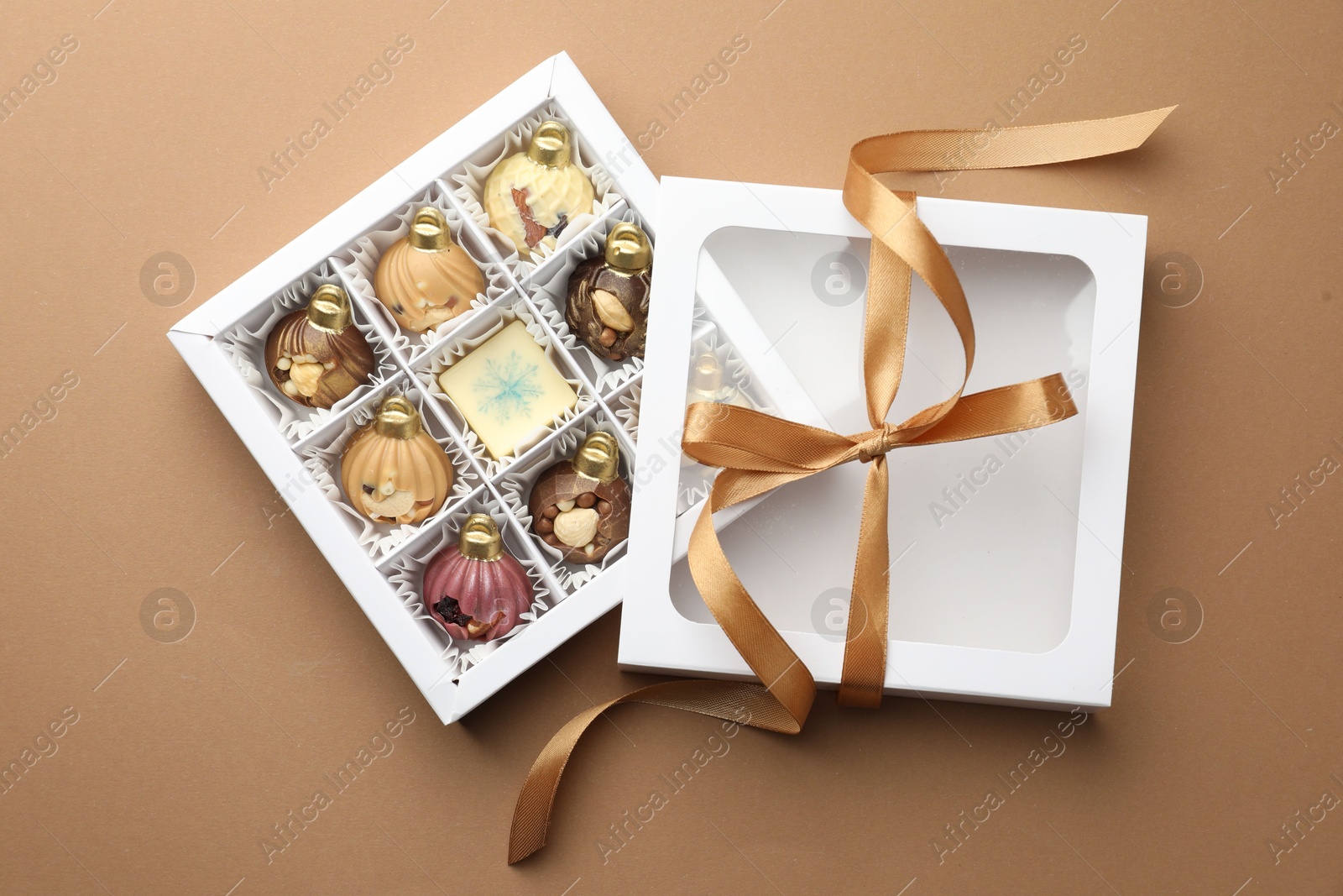 Photo of Open box with delicious chocolate in shape of Christmas ornaments on beige background, top view