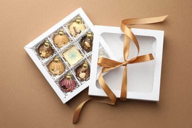 Photo of Open box with delicious chocolate in shape of Christmas ornaments on beige background, top view