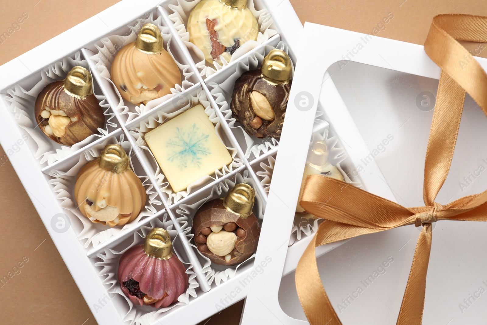 Photo of Open box with delicious chocolate in shape of Christmas ornaments on beige background, top view