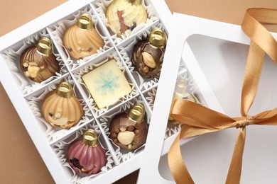 Photo of Open box with delicious chocolate in shape of Christmas ornaments on beige background, top view