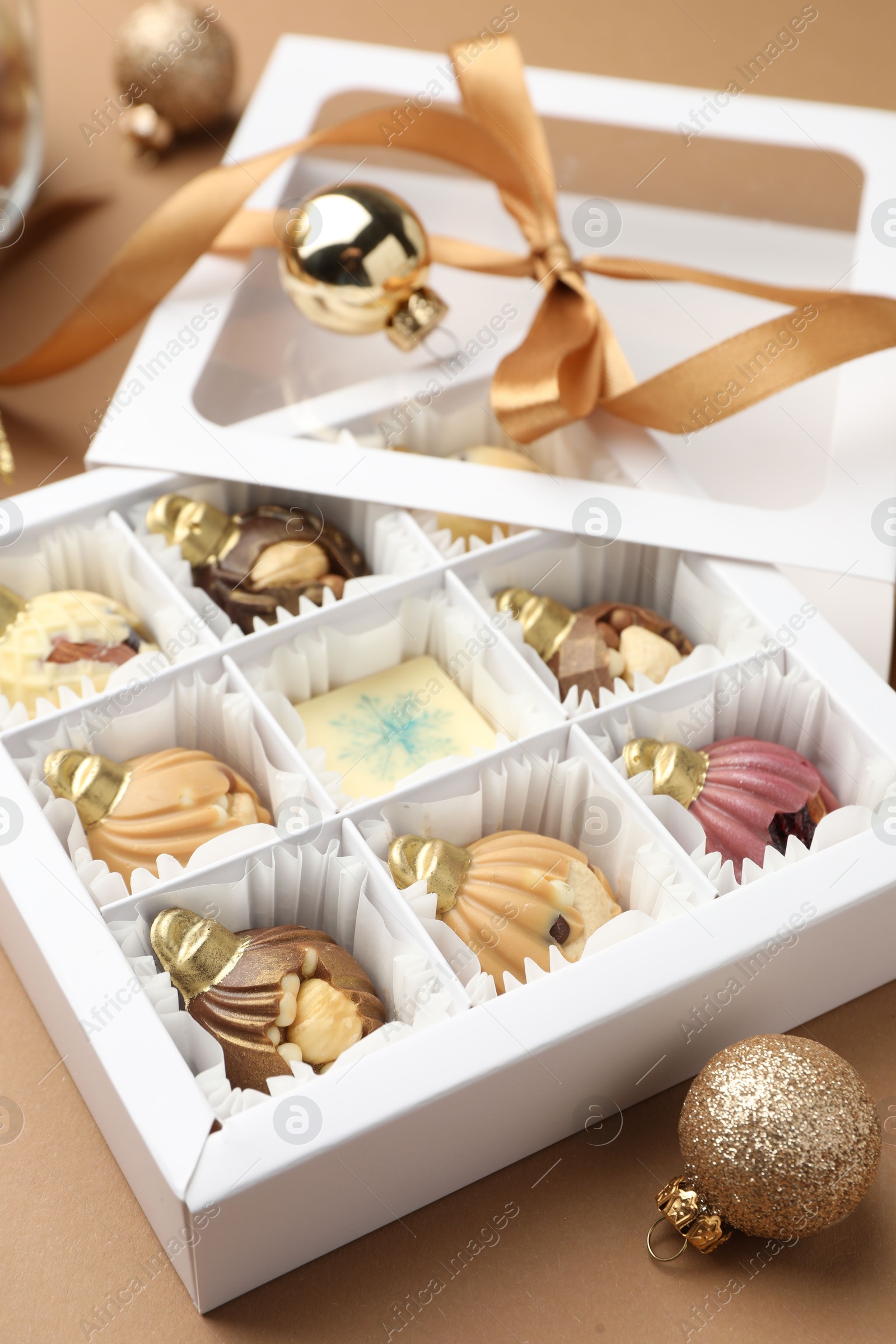 Photo of Delicious chocolate in shape of ornaments in open box and Christmas decor on beige background, closeup