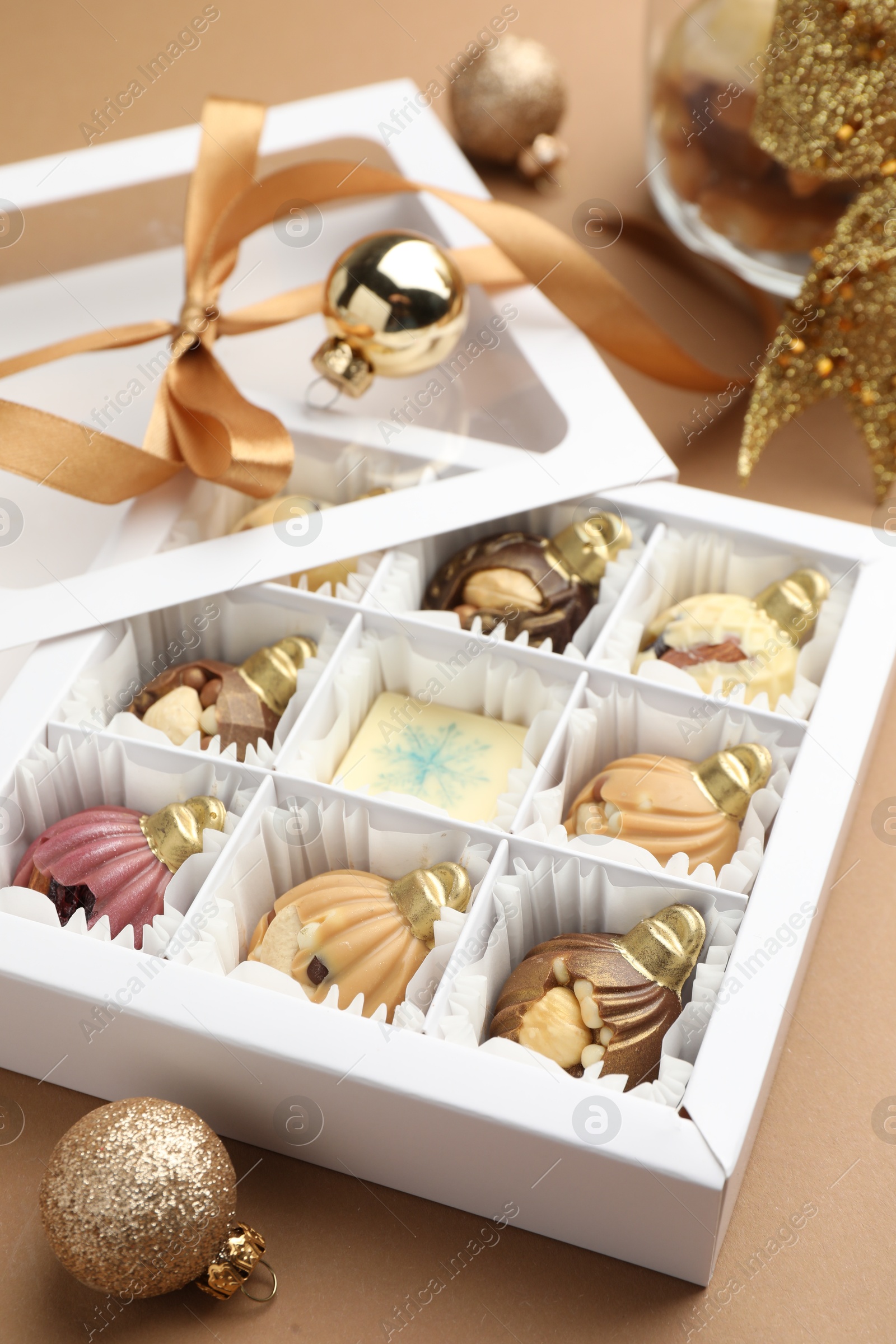 Photo of Delicious chocolate in shape of ornaments in open box and Christmas decor on beige background, closeup