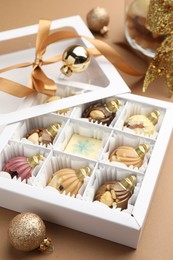 Photo of Delicious chocolate in shape of ornaments in open box and Christmas decor on beige background, closeup