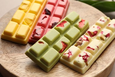 Photo of Different tasty chocolate bars on wooden board, closeup