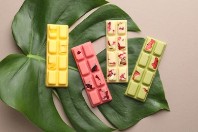 Photo of Different tasty chocolate bars and monstera leaf on beige background, top view