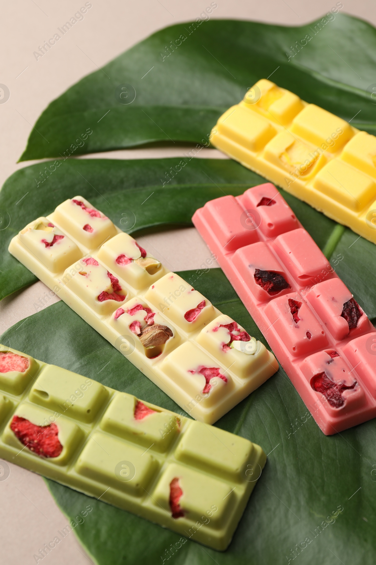 Photo of Different tasty chocolate bars and monstera leaf on beige background, closeup