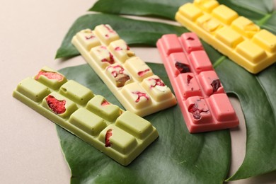 Photo of Different tasty chocolate bars and monstera leaf on beige background, closeup