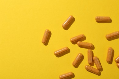 Photo of Many turmeric capsules on yellow background, flat lay. Space for text