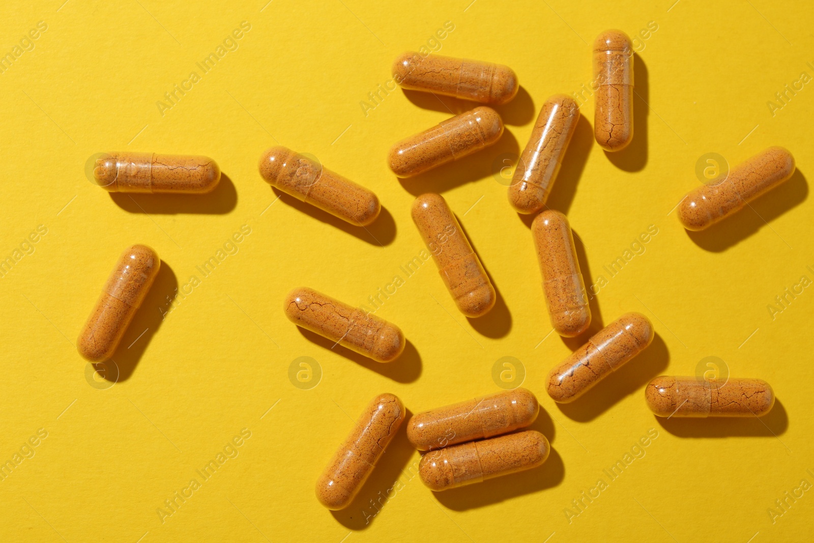 Photo of Many turmeric capsules on yellow background, flat lay