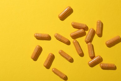 Photo of Many turmeric capsules on yellow background, flat lay