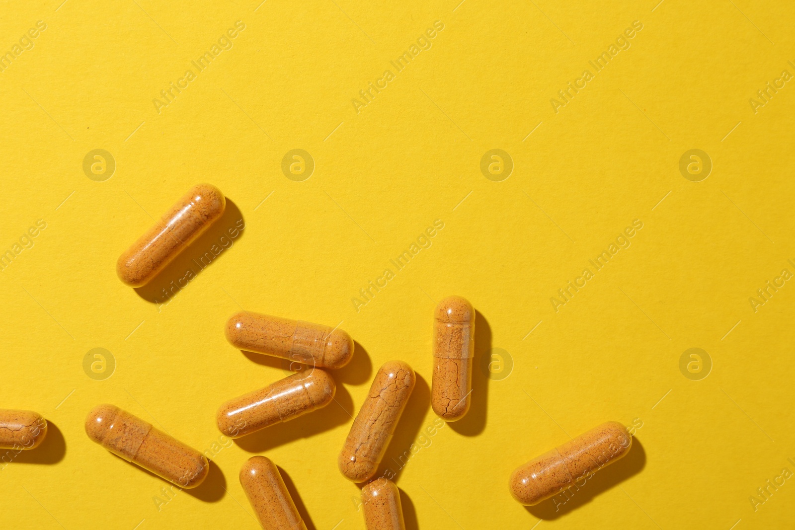 Photo of Many turmeric capsules on yellow background, flat lay. Space for text