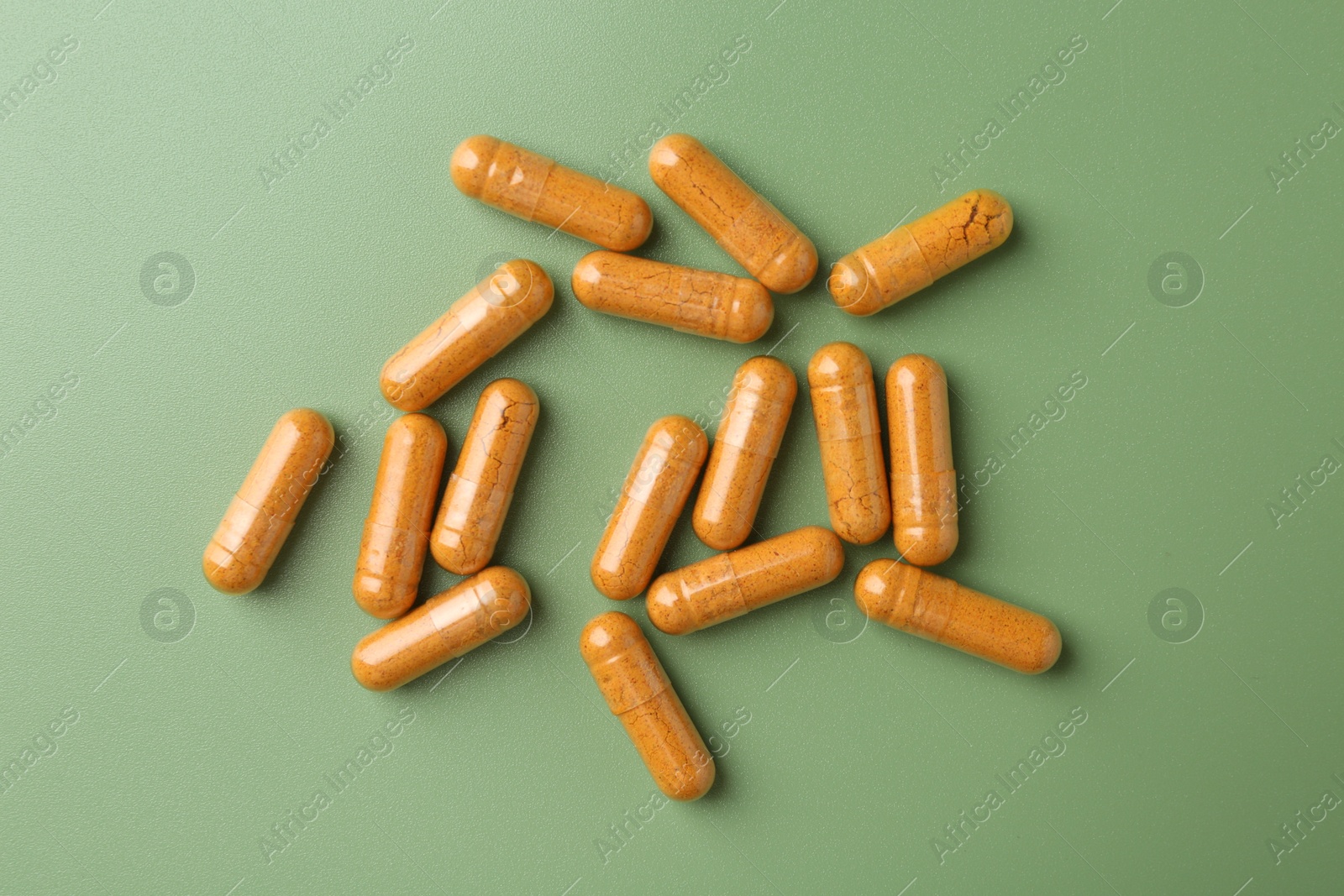 Photo of Many turmeric capsules on light green background, flat lay