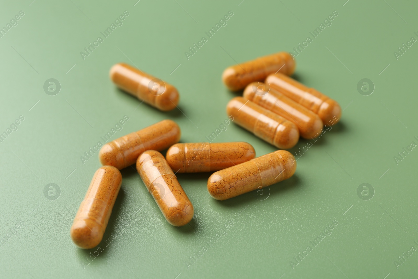 Photo of Many turmeric capsules on light green background, closeup