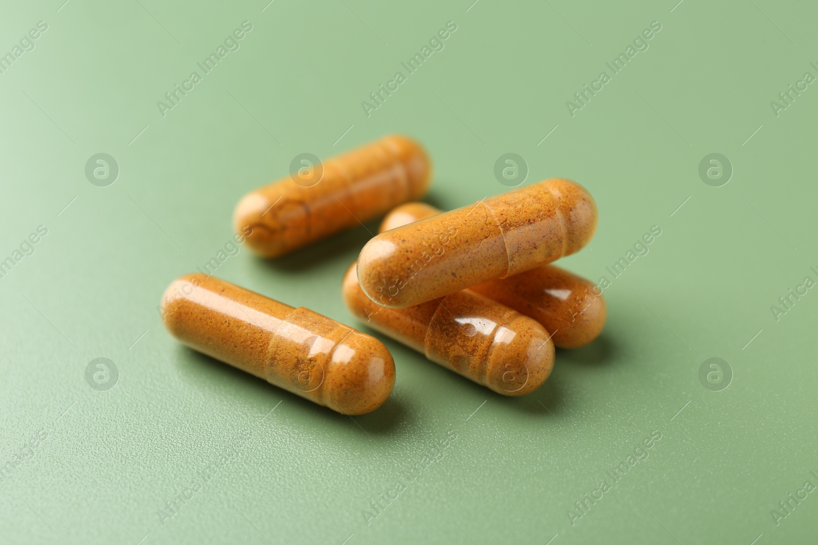 Photo of Many turmeric capsules on light green background, closeup