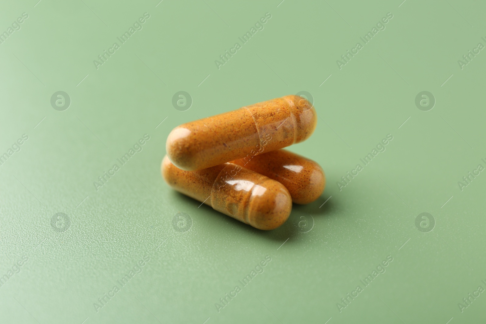 Photo of Many turmeric capsules on light green background, closeup