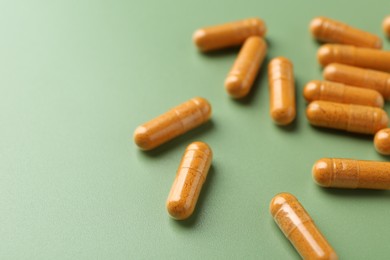 Photo of Many turmeric capsules on light green background, closeup. Space for text