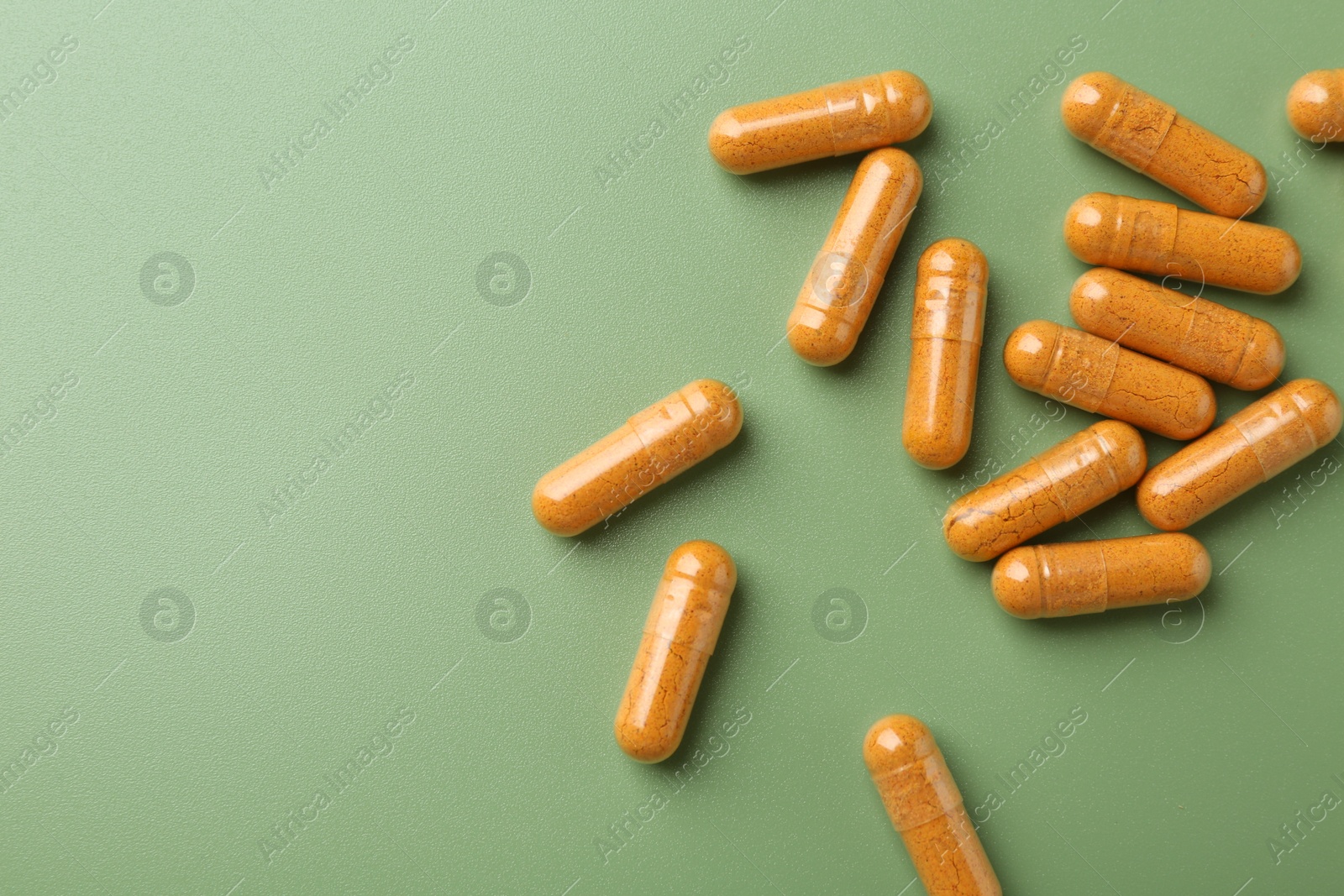 Photo of Many turmeric capsules on light green background, flat lay. Space for text