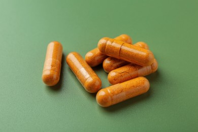 Photo of Many turmeric capsules on light green background, closeup