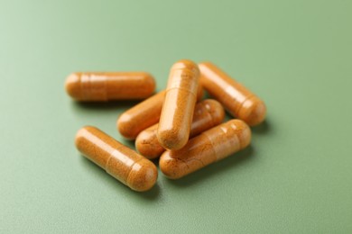 Photo of Many turmeric capsules on light green background, closeup