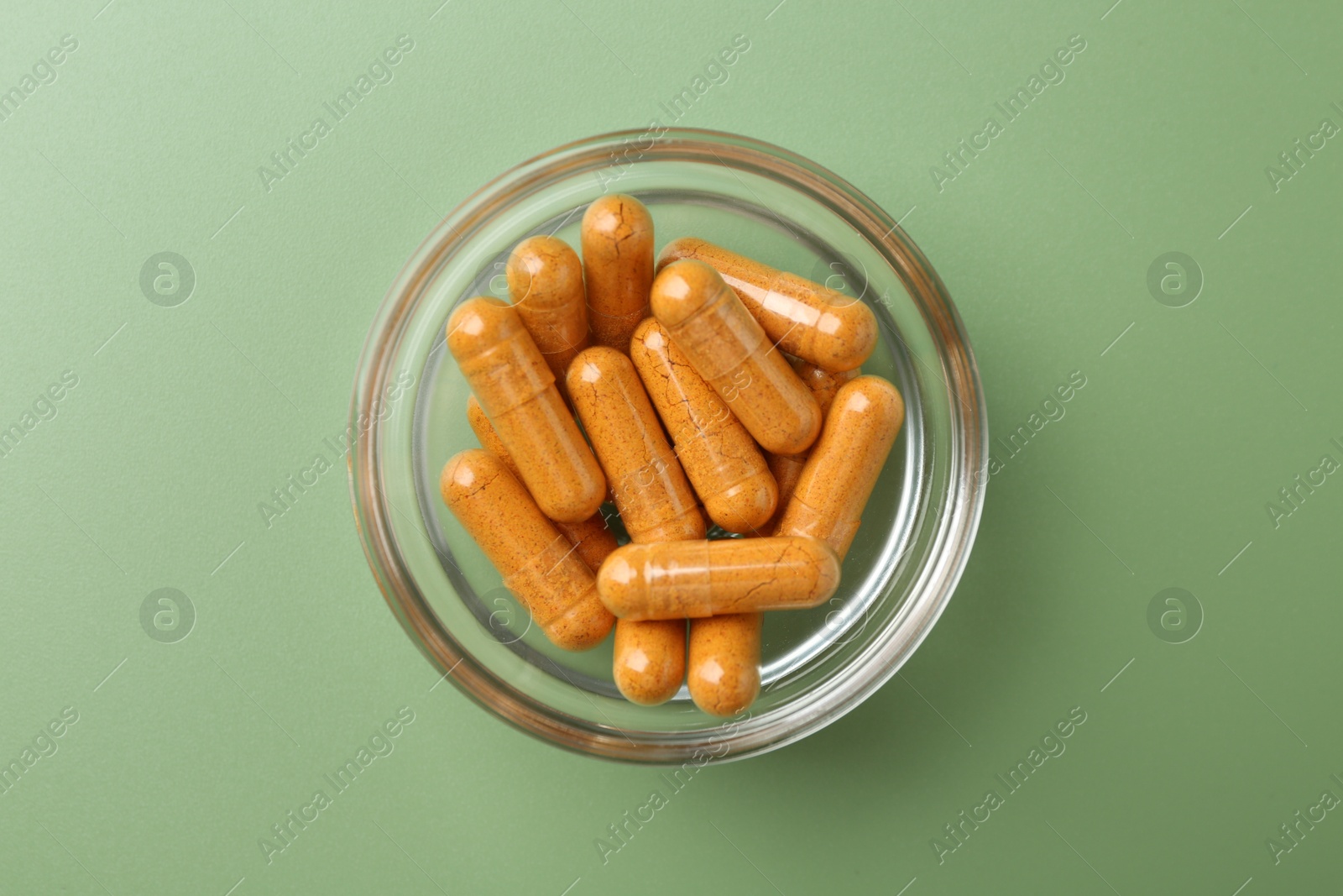 Photo of Many turmeric capsules in bowl on light green background, top view