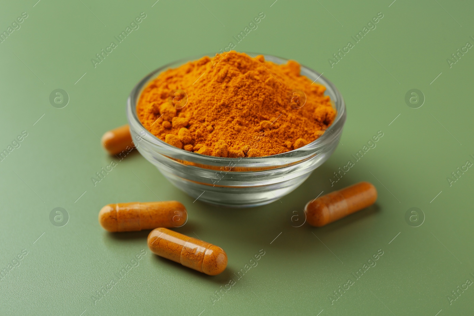 Photo of Many turmeric capsules and powder on light green background, closeup