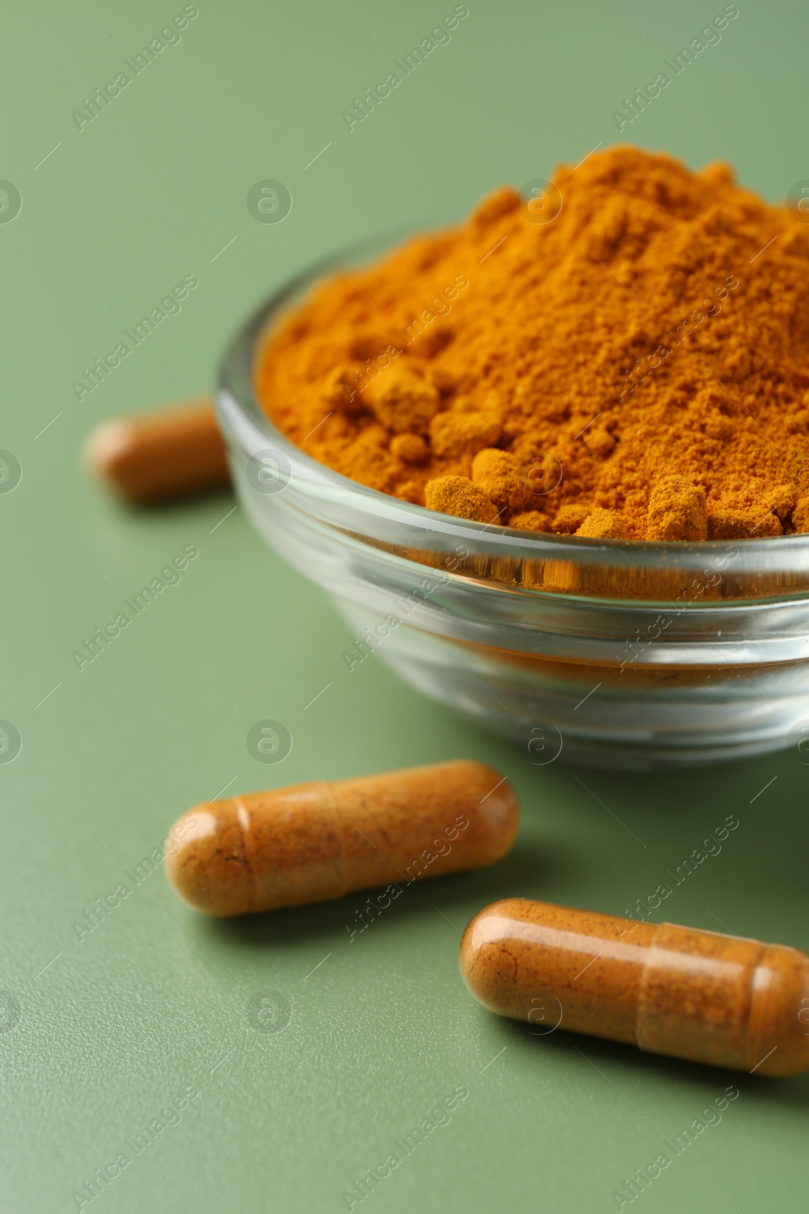 Photo of Many turmeric capsules and powder on light green background, closeup