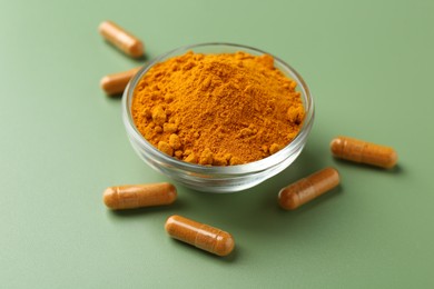 Photo of Many turmeric capsules and powder on light green background, closeup