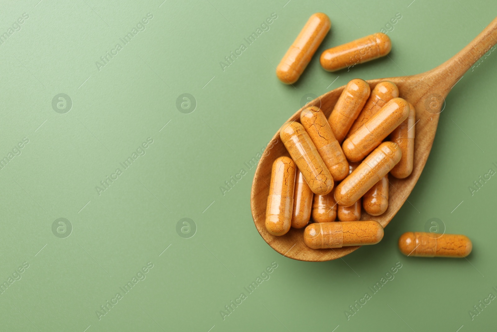 Photo of Turmeric capsules in spoon on light green background, top view. Space for text