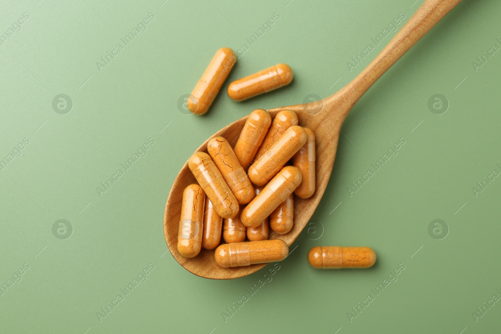 Photo of Turmeric capsules in spoon on light green background, top view