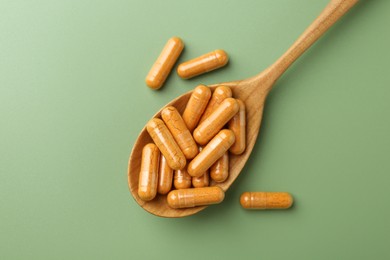 Photo of Turmeric capsules in spoon on light green background, top view