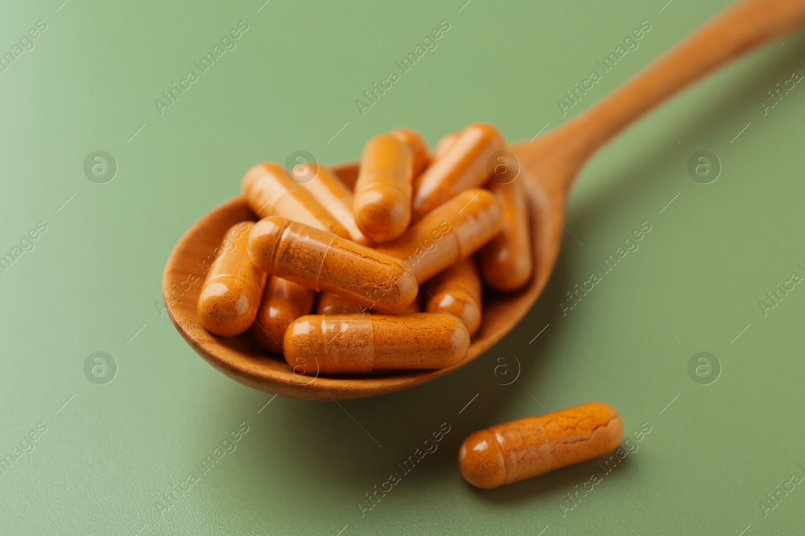 Photo of Turmeric capsules in spoon on light green background, closeup