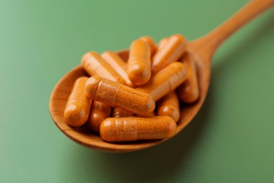 Photo of Turmeric capsules in spoon on light green background, closeup