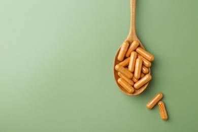 Photo of Turmeric capsules in spoon on light green background, top view. Space for text